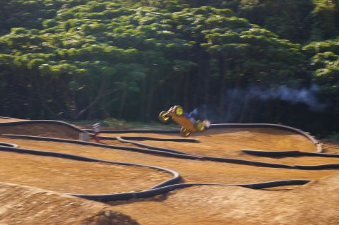1986 Ford Bronco - A remote control buggy takes flight over a dirt track, kicking up dust and smoke.