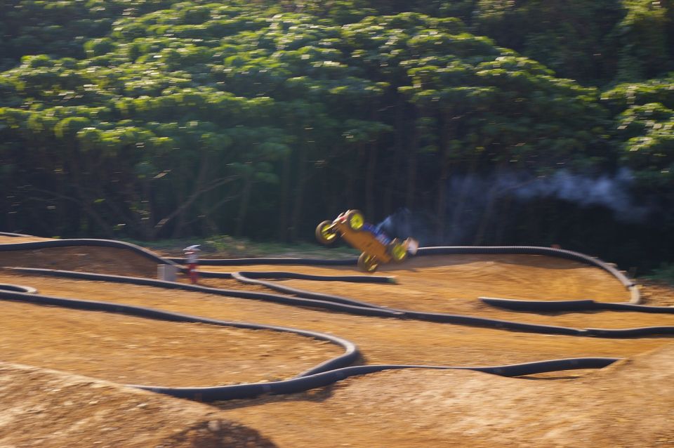 Yellow remote control buggy airborne over a dirt track, emitting smoke