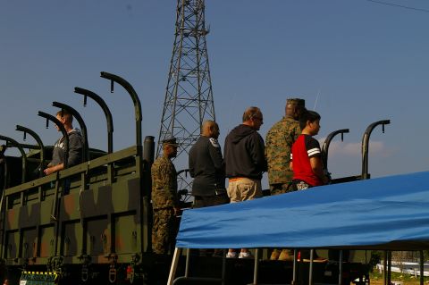 1986 Ford Bronco - Several individuals, some in military uniform, are standing on the bed of a camouflage truck.