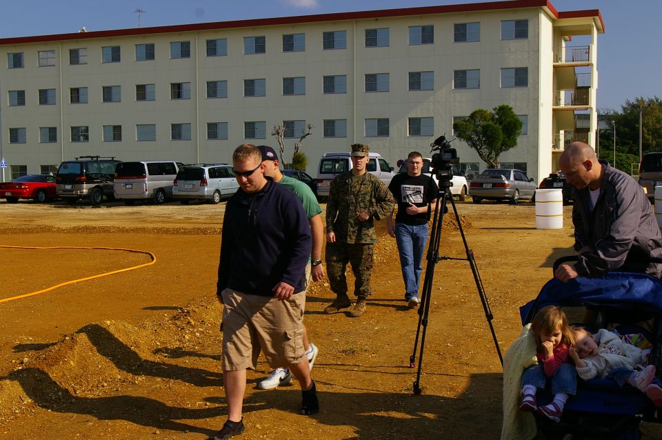 Several vehicles parked in front of a building, with people walking in the foreground
