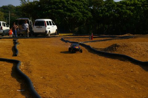 1986 Ford Bronco - A remote control buggy navigates a dirt track with several vans parked in the background.
