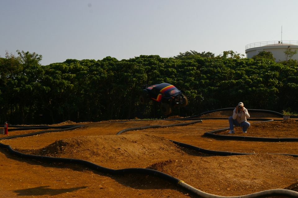 RC car mid-air over dirt track, person crouching to take photo