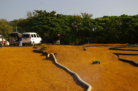 1986 Ford Bronco - A remote control car navigates a dirt track with several vans parked nearby under a line of trees.