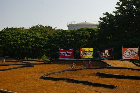 1986 Ford Bronco - An outdoor RC car track is set up with various sponsor banners in the background under a clear sky.