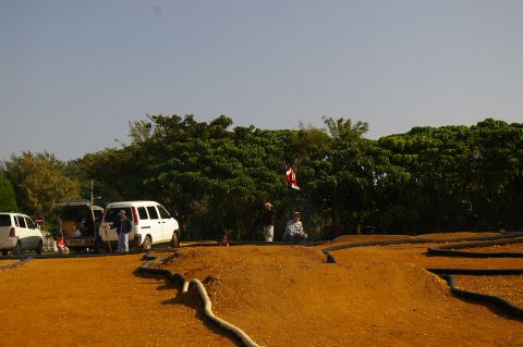 1986 Ford Bronco - People gather at an RC car track with vans parked nearby under a clear sky.