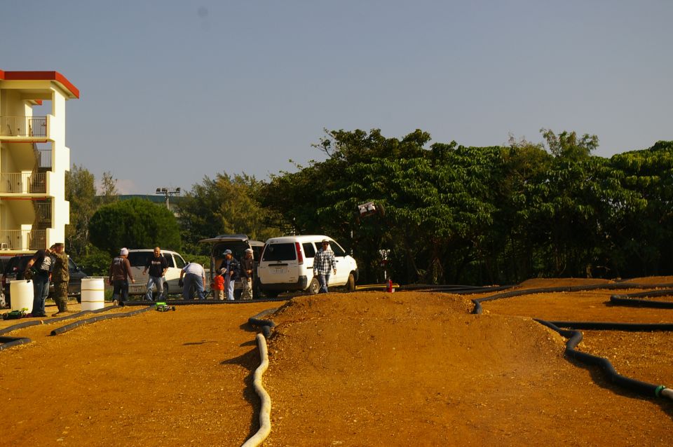 People gathered around vans near a dirt track with remote control cars