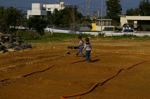 1986 Ford Bronco - Two young boys walk across a dirt track, one with a remote control car, with orange hoses marking the course.