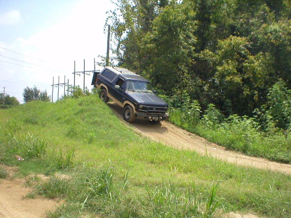 Dark blue Ford Bronco descending a steep dirt hill onto a gravel trail