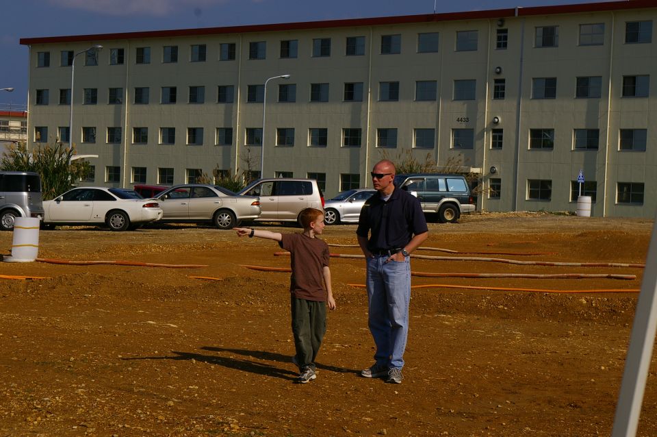 Dirt lot with two people and parked cars in front of a building. Building has address 4433