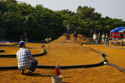 1986 Ford Bronco - A group of people watch remote control cars race on a dirt track with a wooded background.