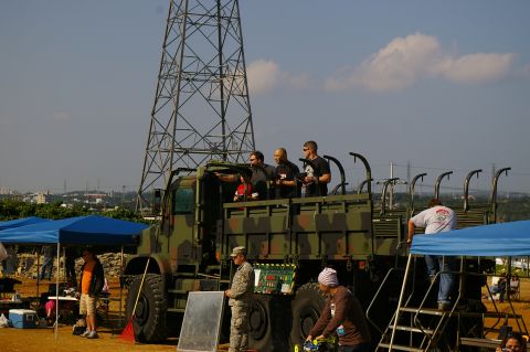 1986 Ford Bronco - A camouflage military truck is parked outdoors with several people standing in its cargo bed.