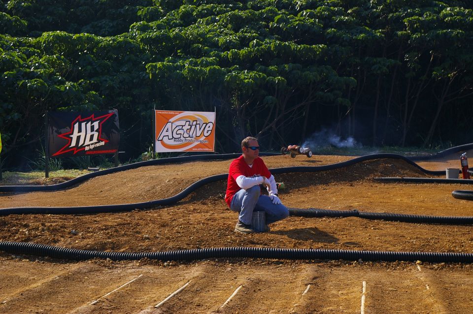 Remote control car kicking up dust on a dirt track, with a man watching