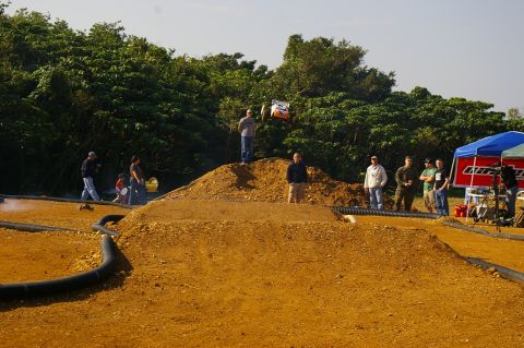 1986 Ford Bronco - Spectators watch a remote control car perform a jump on a dirt track during an event.