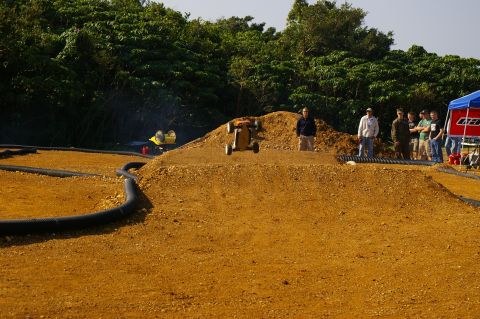 1986 Ford Bronco - RC buggy jumps a dirt track while spectators observe the race.