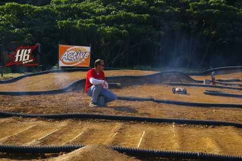 1986 Ford Bronco - A man observes a remote control car race on a dirt track, with sponsor banners visible behind him.