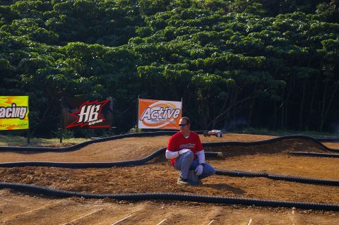 1986 Ford Bronco - A man watches a remote control car navigate a dirt track with sponsor banners in the background.