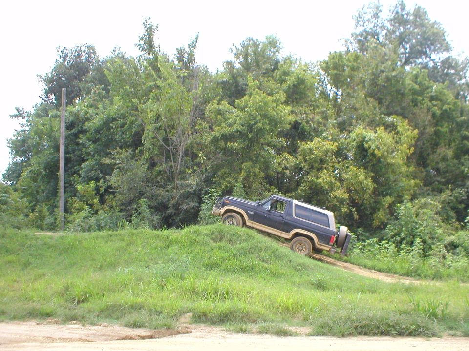 Dark blue two-door Bronco SUV climbing down a steep grassy dirt mound off-road