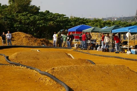 1986 Ford Bronco - Spectators gather around a dirt track set up for remote control car racing, with tents providing shade.