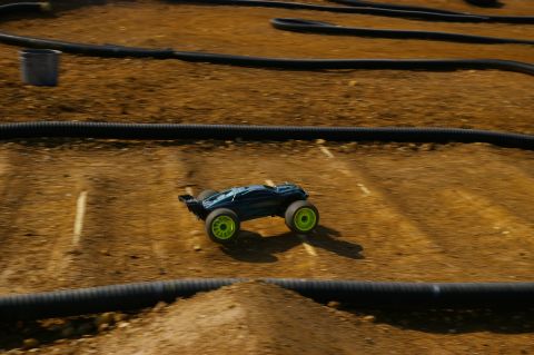 1986 Ford Bronco - RC buggy races on a dirt track with black tubing lining the course.