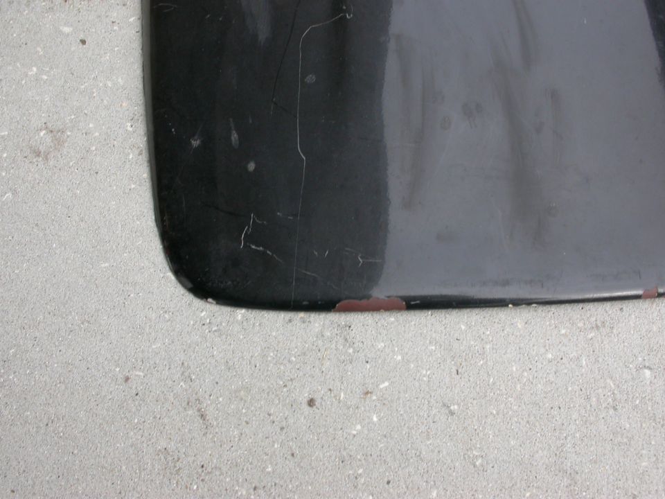 Black car part with chipped paint, on concrete. Supermotors.net logo visible