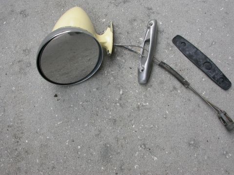 1968 Mercury Cougar - A car side mirror assembly, including the mirror, mounting bracket, and gasket, lies on a concrete surface.