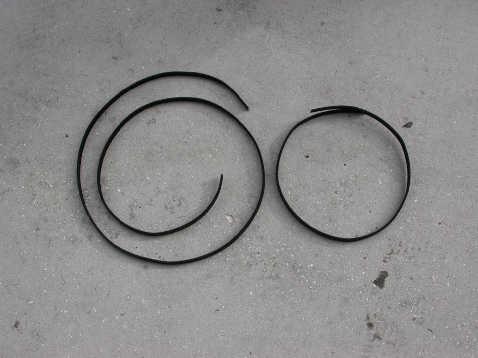 Two black rubber trim pieces, one coiled and one circular, on a concrete surface