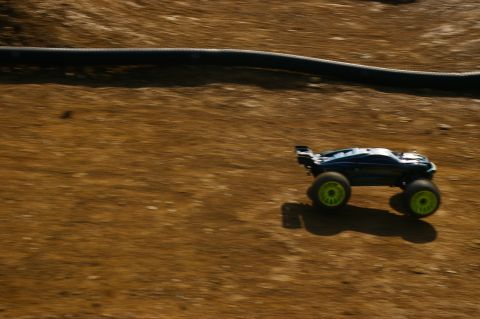 1986 Ford Bronco - A remote control monster truck is captured in motion on a dirt track, its bright green wheels a blur against the brown terrain.