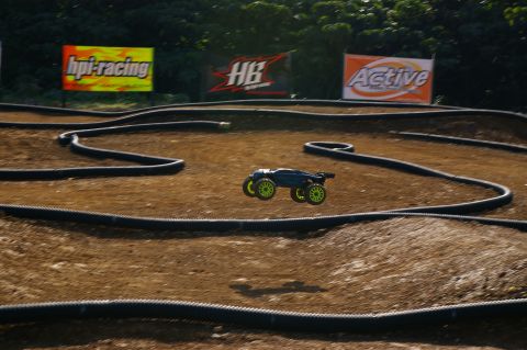 1986 Ford Bronco - A remote control car jumps over a dirt track with advertising banners in the background.
