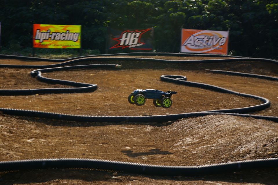 Blue remote control car with neon green wheels in mid-air over a dirt track