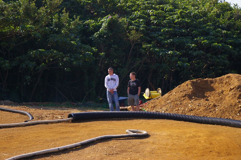 two guys standing by a dirt track with a yellow remote control car in the background