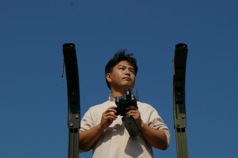 1986 Ford Bronco - A man holds a remote control device while looking upwards, framed by two tall, dark structures.