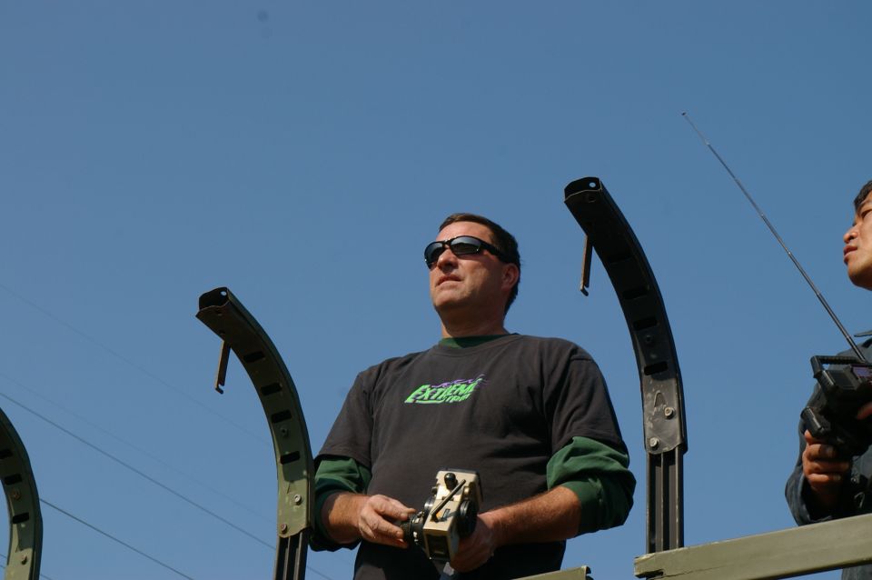 Man in sunglasses holds a remote control, wearing a black t-shirt with green trim