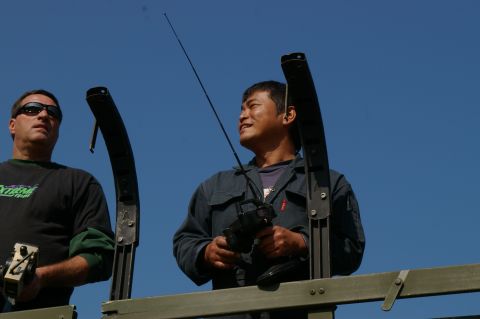 1986 Ford Bronco - Two men appear to be operating remote-controlled devices, possibly for a hobby or event, against a clear blue sky.
