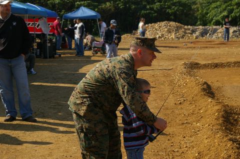 1986 Ford Bronco - Marine assists child with fishing rod at an outdoor event with tents and spectators.