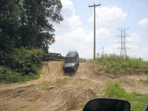 1983 Ford Bronco - Two SUVs navigate a challenging muddy terrain with power lines overhead.