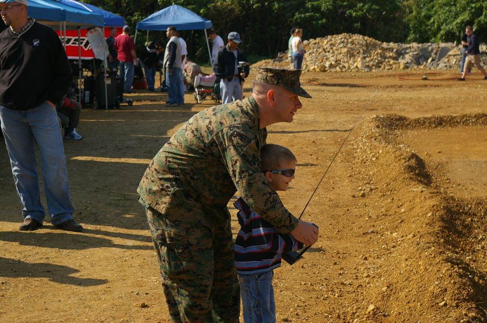 Marine helps a kid control a remote-controlled car on a dirt track