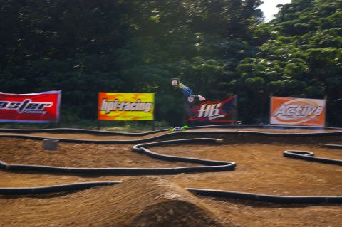 1986 Ford Bronco - Remote control buggy jumps on a dirt track with sponsor banners visible.