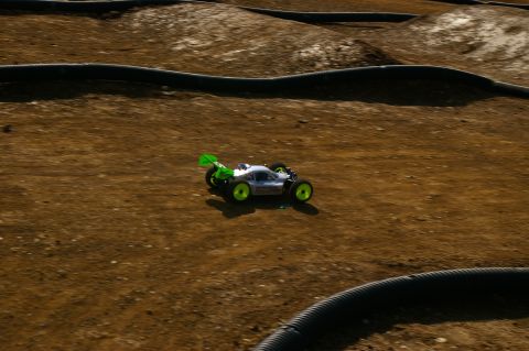 1986 Ford Bronco - A remote control buggy races on a dirt track with black tubing along the edges.