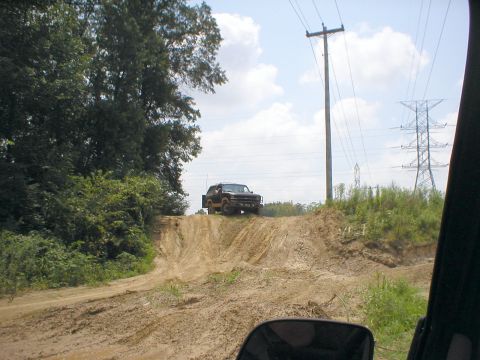 1983 Ford Bronco - A truck navigates a challenging dirt track under a partly cloudy sky.