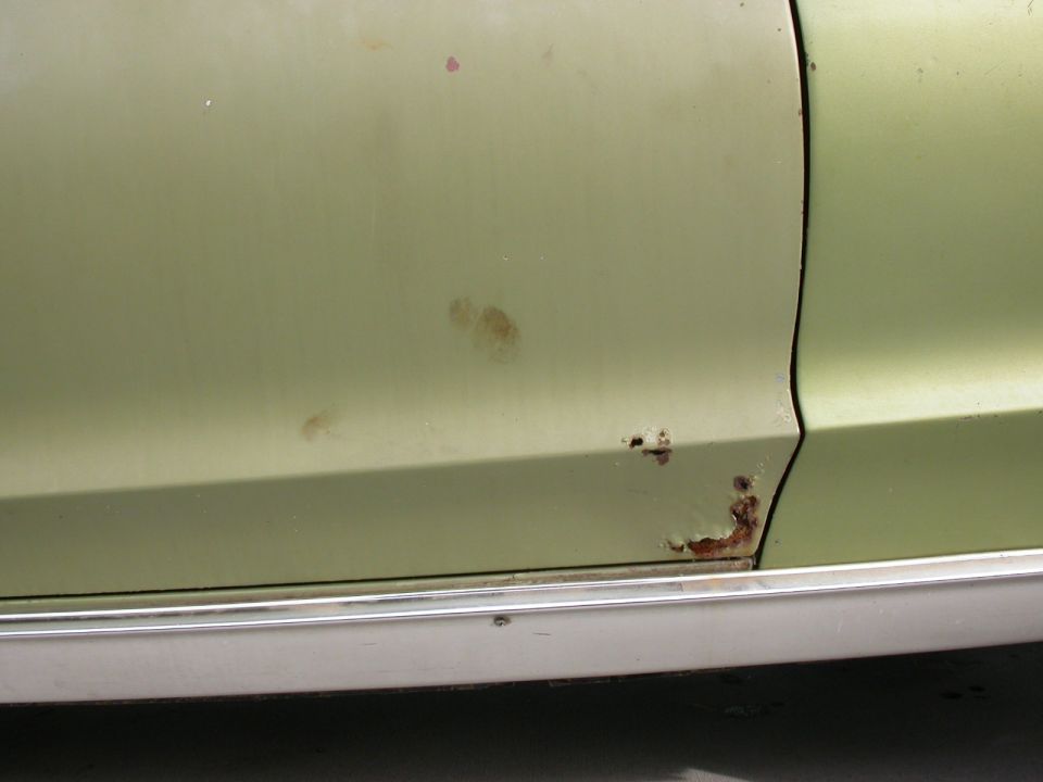 Light green car door with rust near the bottom and chrome trim