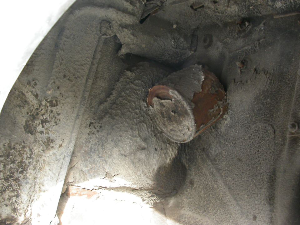 Underside of a vehicle's wheel well showing rust and grime on metal components