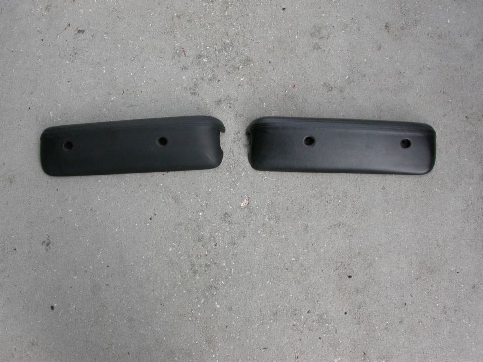 Two black plastic trim pieces with two screw holes each, lying on a concrete surface