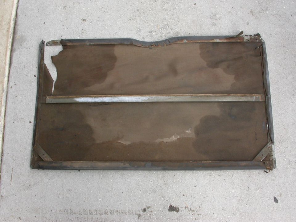 Damaged car door panel with torn fabric and rusted metal frame, lying on concrete