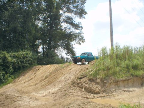 1983 Ford Bronco - A teal pickup truck navigates a dirt track on a sunny day.