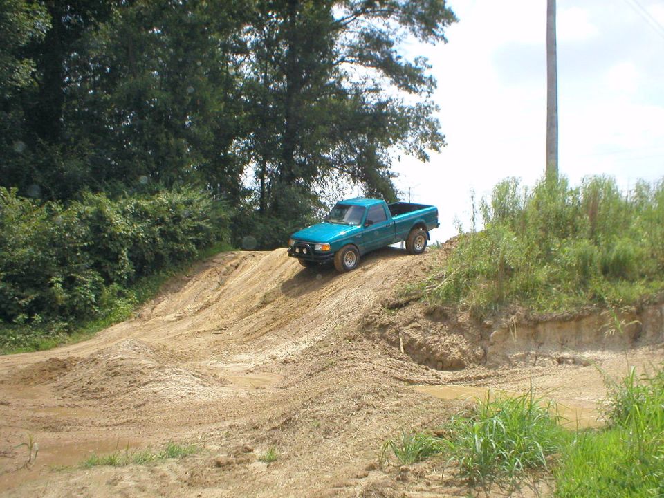 Teal pickup truck perched at top of steep dirt hill at off-road course
