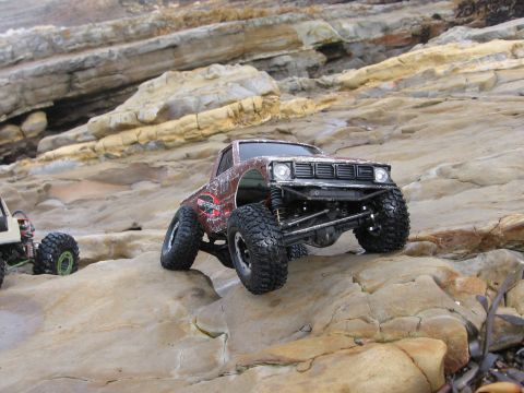 1993 Toyota 4Runner - A toy rock crawler truck navigates a rocky coastal landscape, with another RC vehicle visible in the background.