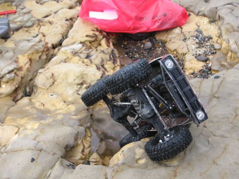 1993 Toyota 4Runner - A toy truck is overturned on a rocky shore, with a red bag in the background.