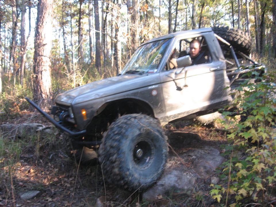 1984 Ford Bronco II modified for off-roading, climbing over rocks on a wooded trail