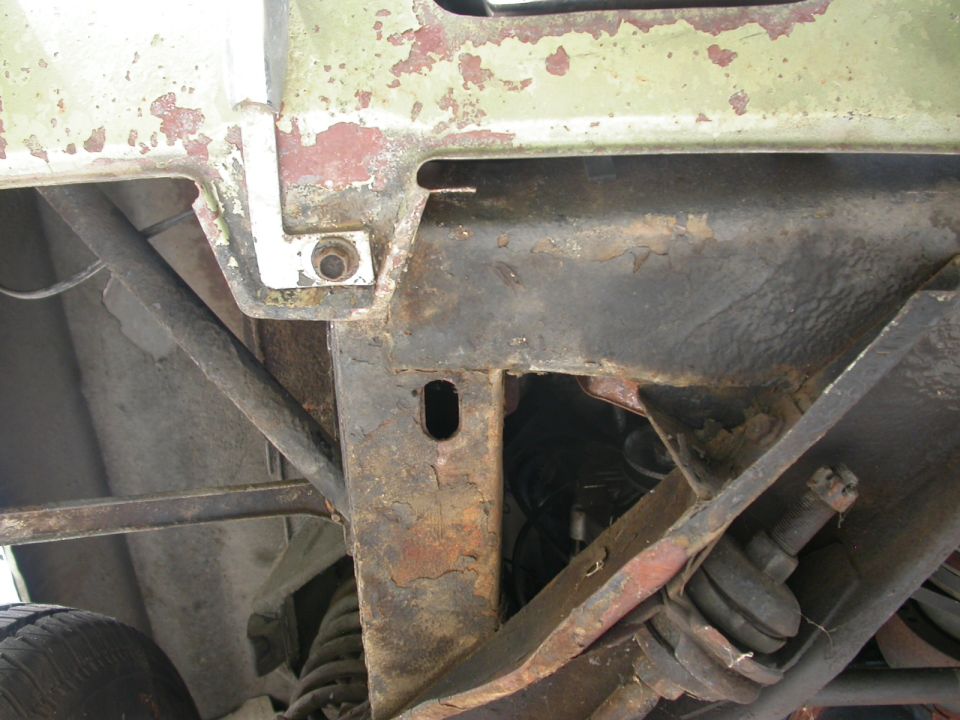 rusted vehicle frame, suspension components, and part of a tire visible from underneath