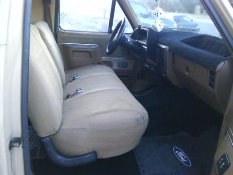 1990 Ford Bronco - The interior of this 1990 Ford Bronco features a tan bench seat and dashboard, with a Ford logo visible on the floor mat.